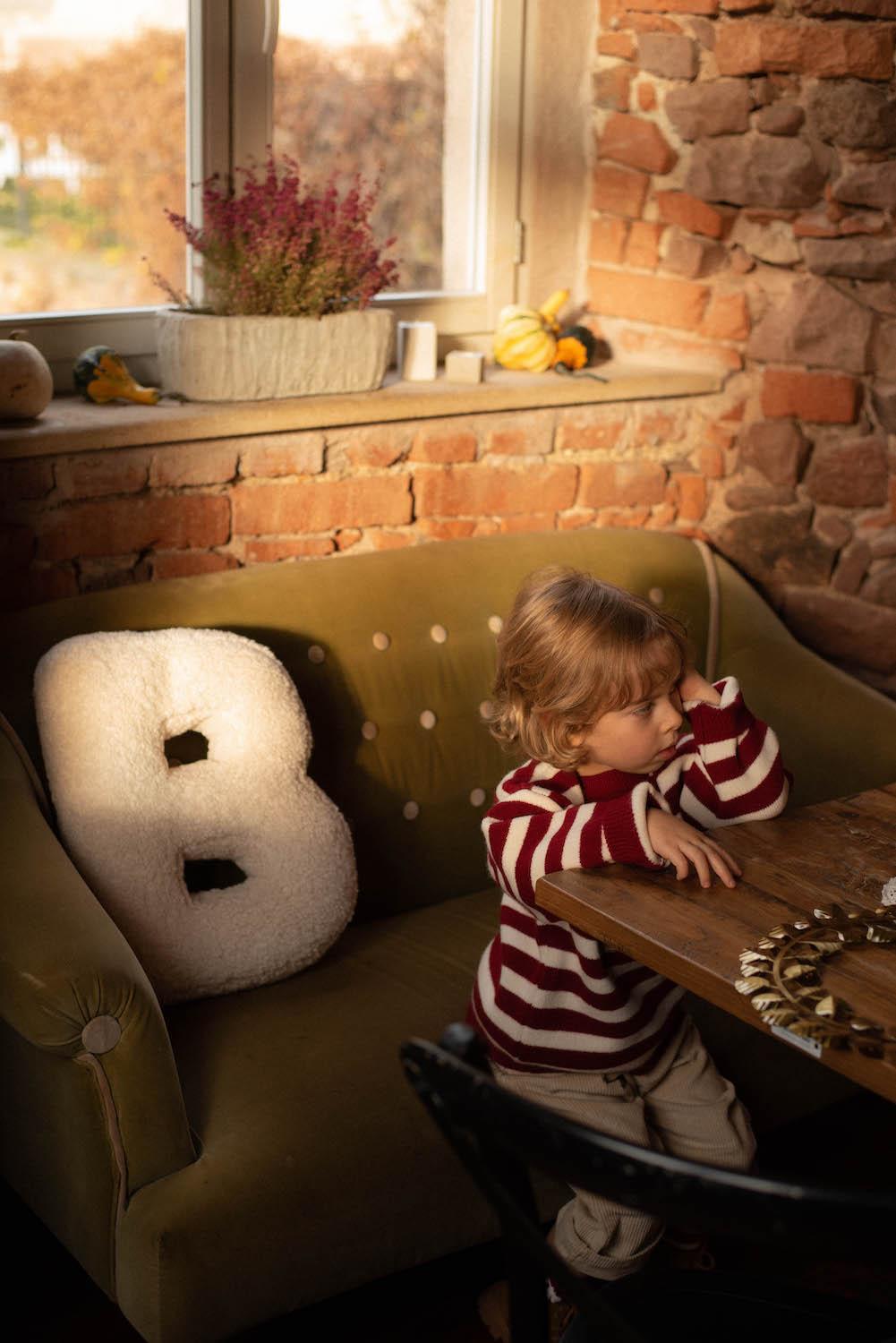 Boucle Letter Cushion B Teddy Letter Pillow by Bettys Home on sofa next to young boy in red stipe sweater