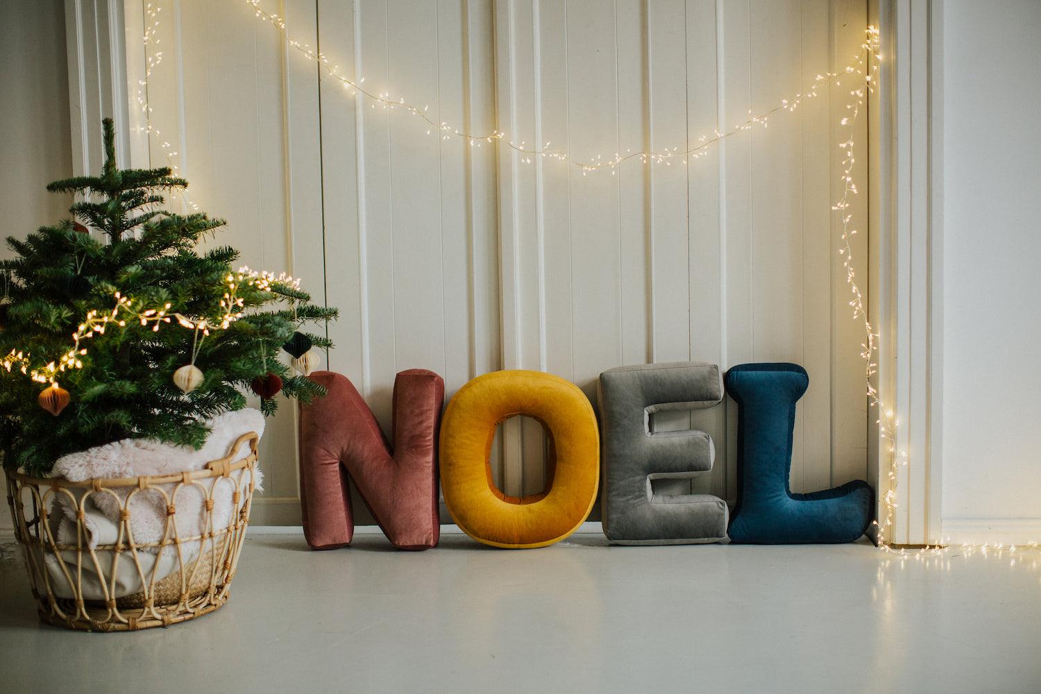 Velvet letter cushions from bettys home arranged in the word NOEL next to the Christmas tree