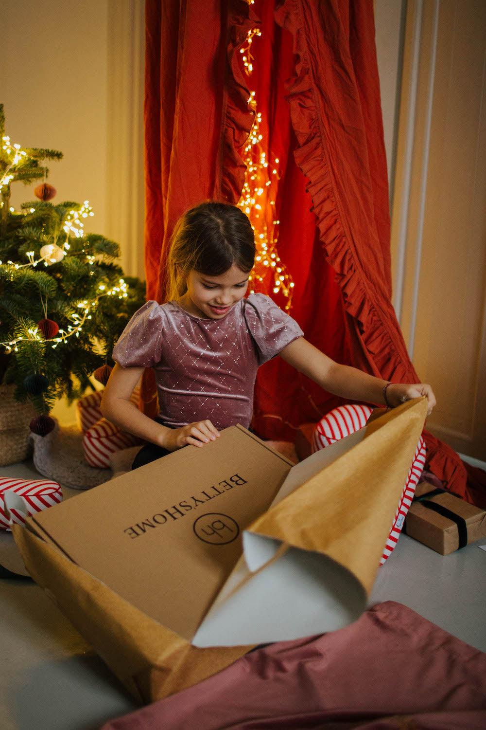a girl opening an gift next to Christmas tree with velvet letter cushion by bettys home inside