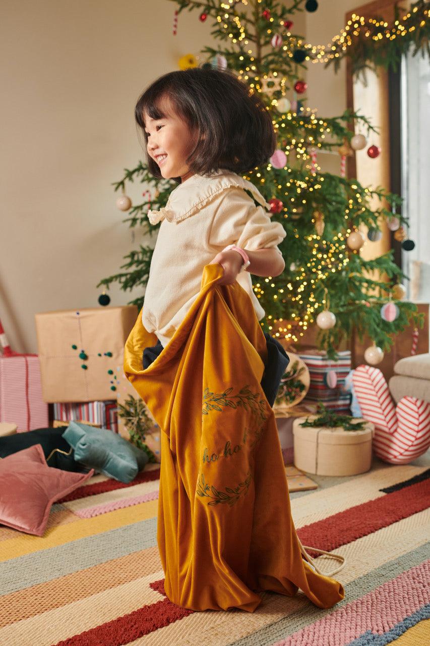 small cute girl standing in yellow christmas gift sack by bettys home during christmas time