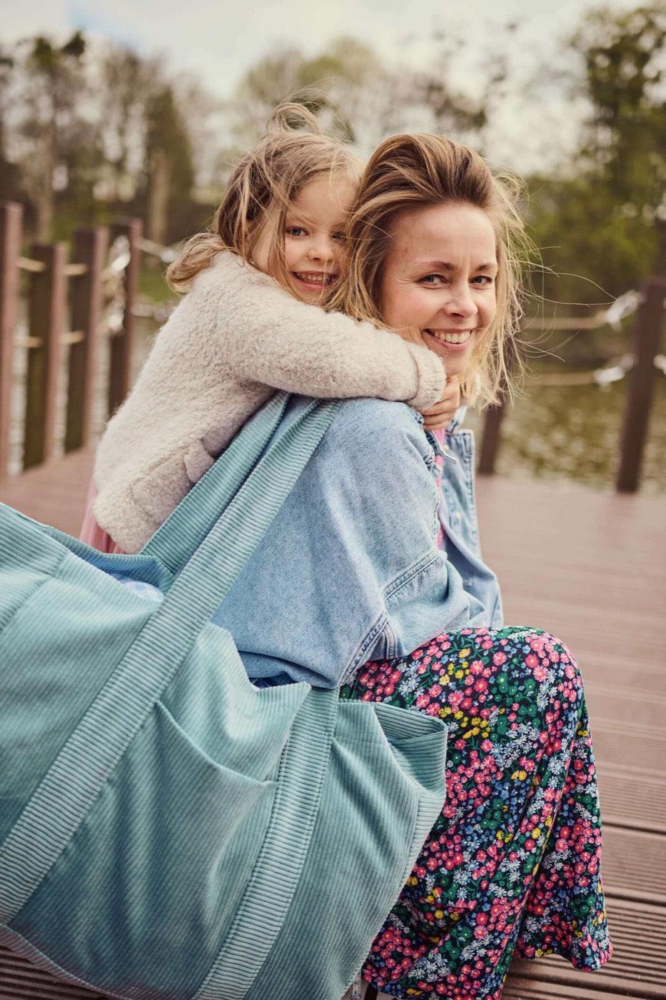 Happy mom with her daughter. She has blue corduroy mom bag with her by betty's home