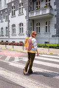 A young woman in the city crossing the lanes with a red gingham backpack for laptop. checkered handbag backpack