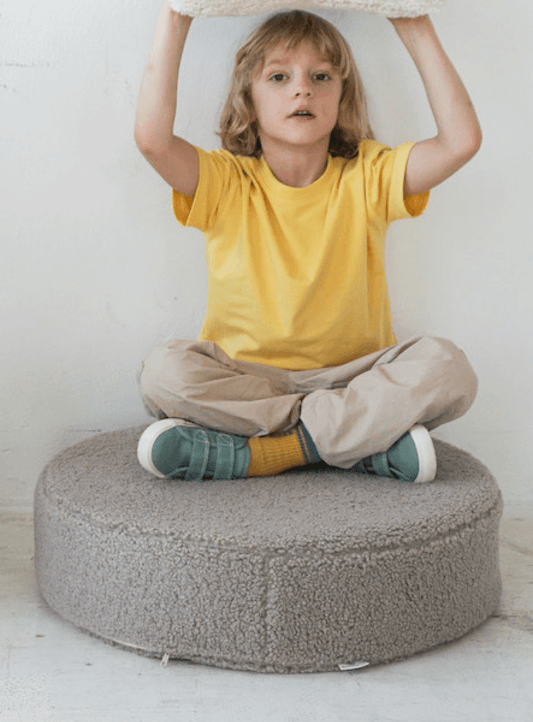 a boby in yellow t-shirt sitting on large boucle pouf in taupe bay bettys home.