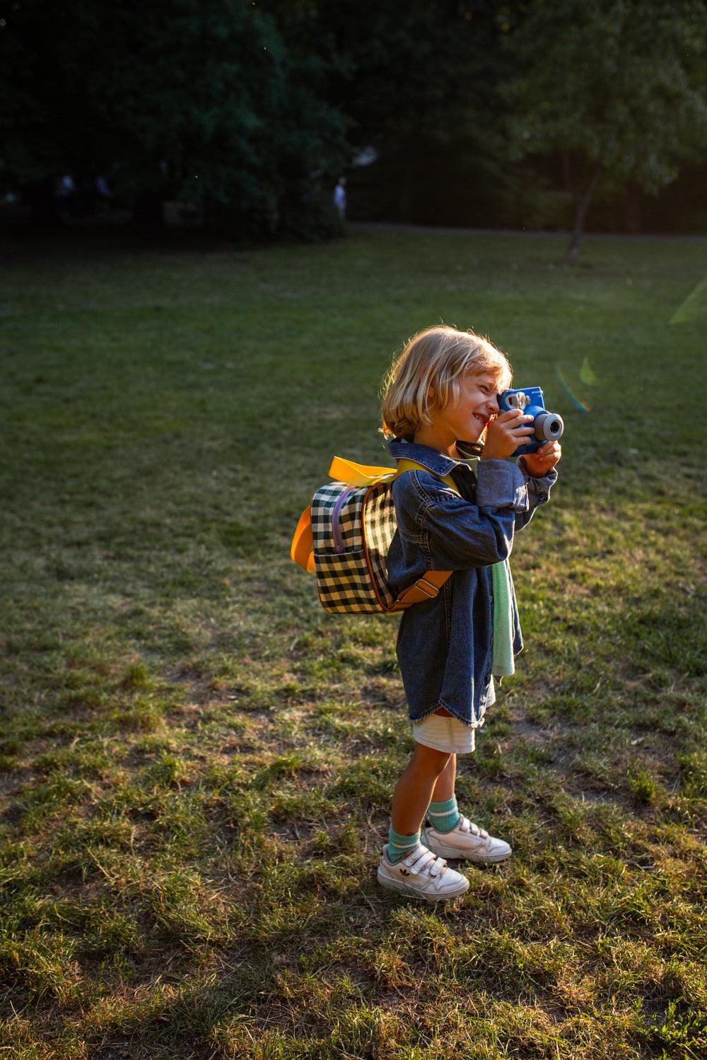 cute boy with photo camera and green small checkered backpack. gingham backpack for kindergarten