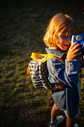 a little boy with a small gingham backpack pretends to take pictures with a toy camera. small checkered backpack