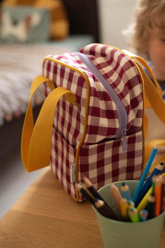 Small checkered backpack for kids standing on desk. Gingham red backpack