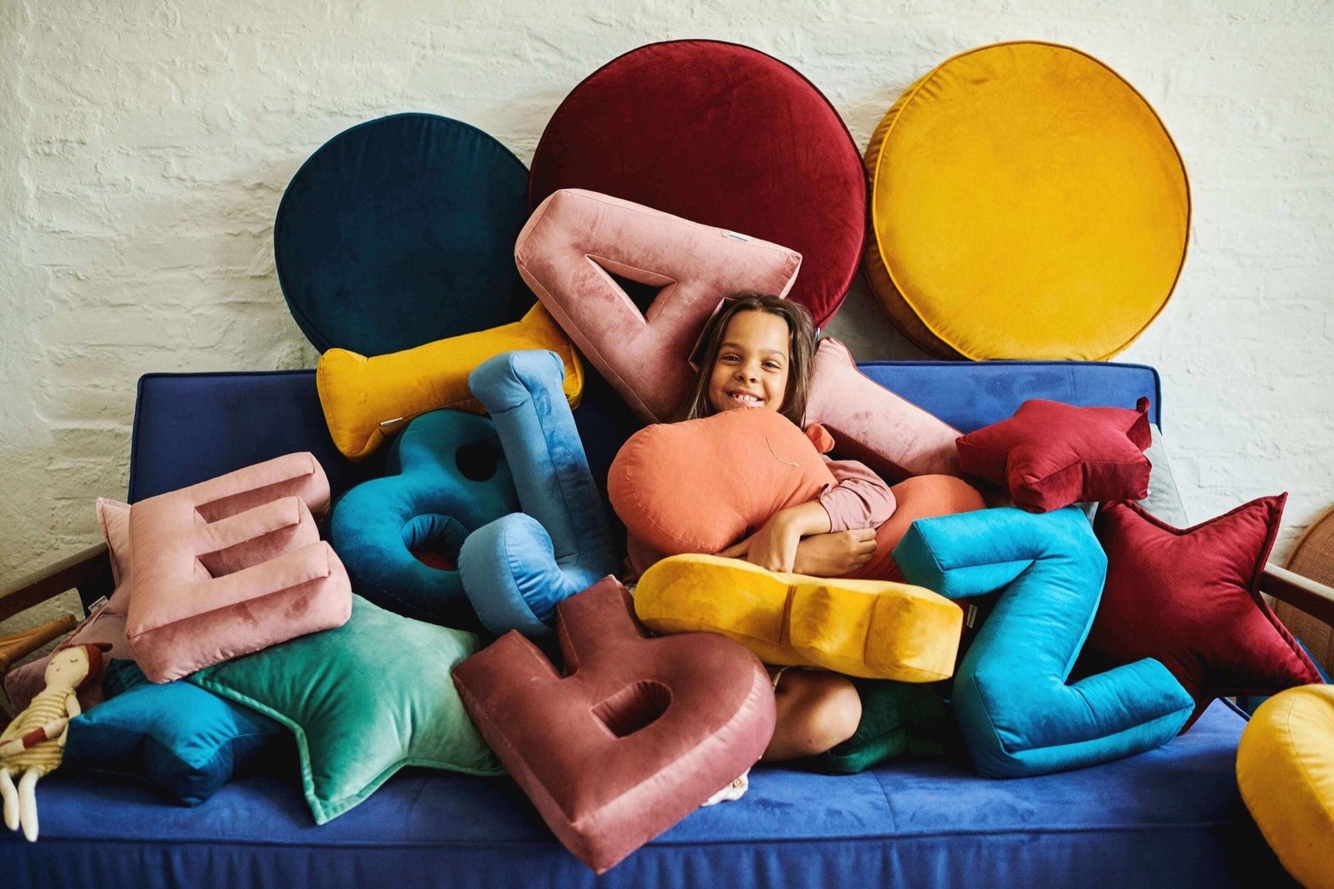 cute girl sitting on sofa under many velvet letter cushions by Bettys home