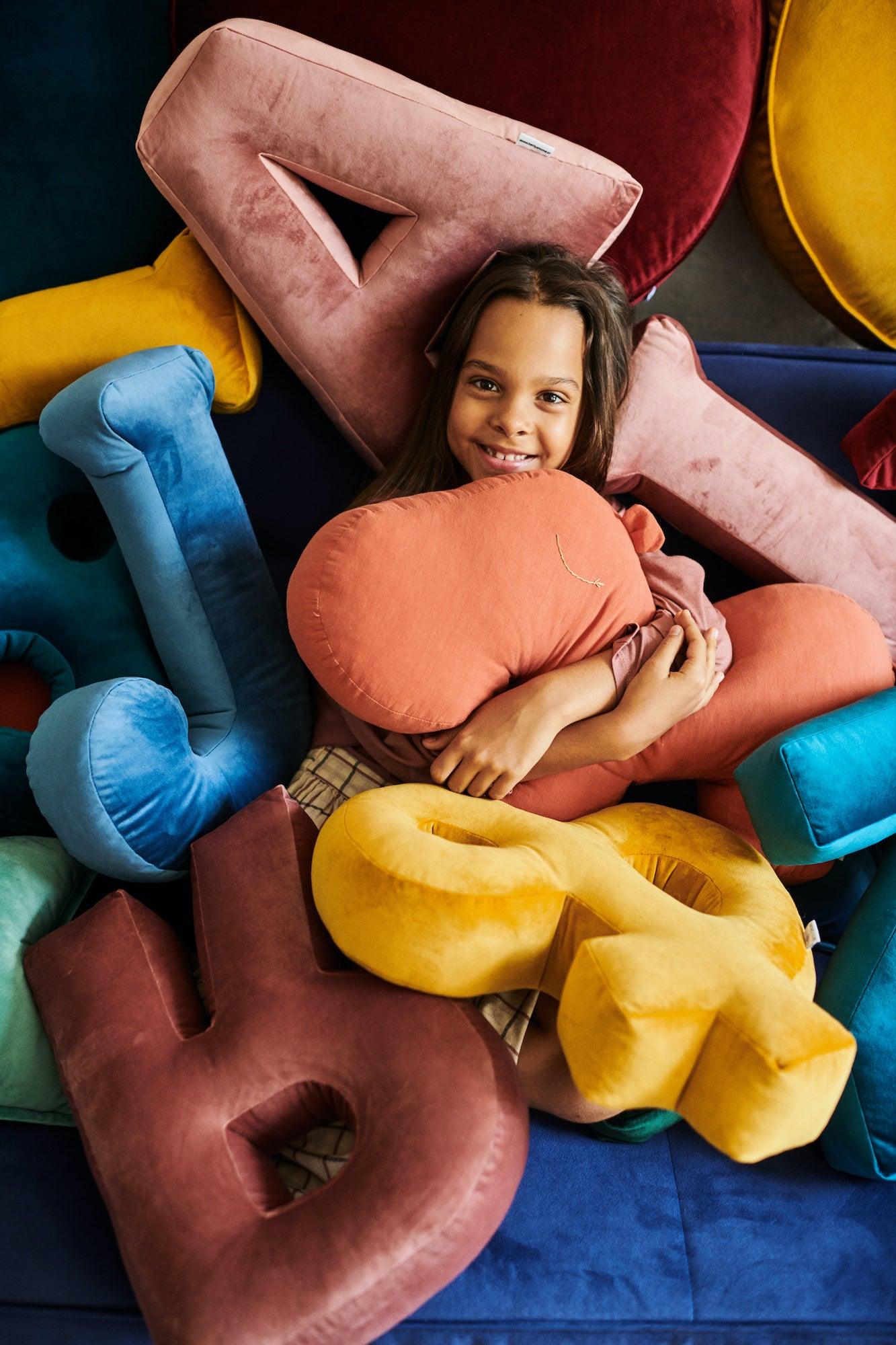 cute girl under lot of velvet letter cushions and cotton hippo pillow by bettys home