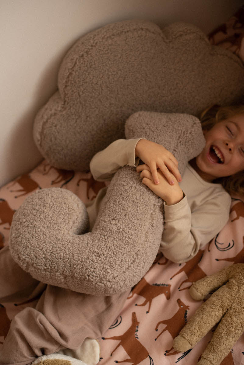 little boy lying and laughing on bed with boucle letter cushion J mocha