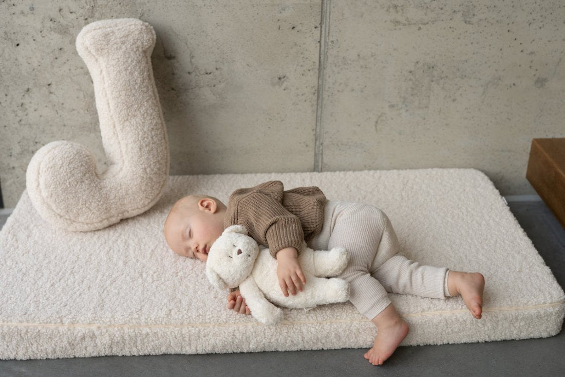 little boy lying on a boucle mattress next to a cream boucle letter cushion from bettys home, teddy boucle mattress for modern nursery
