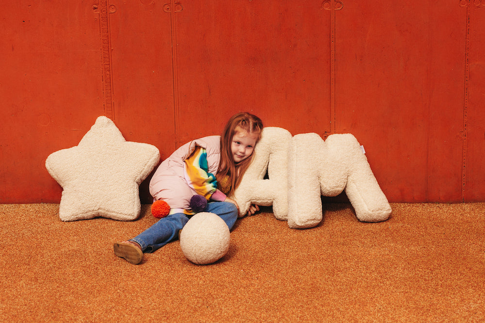 girl sitting on playground wit boucle star cushion and boucle letter cushions. teddy star cushion