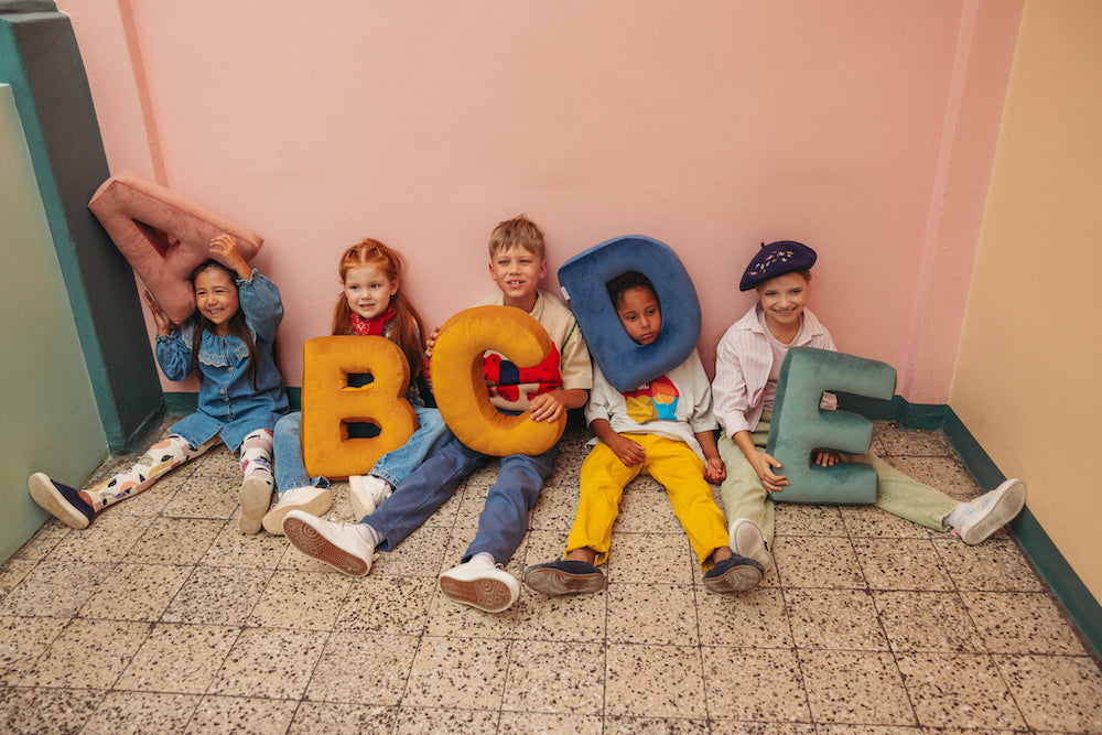 kids sitting on floor at school with velvet letter cushions by bettys home. letter shaped pillow