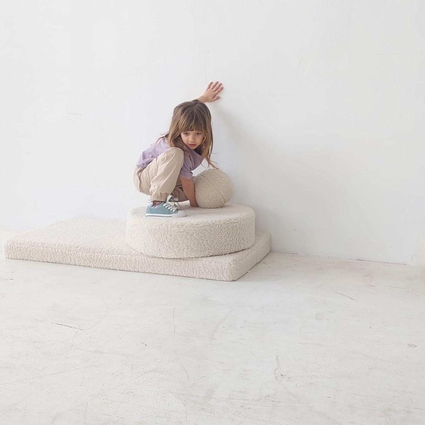 girl standing on boucle mattress with boucle ball in hands 