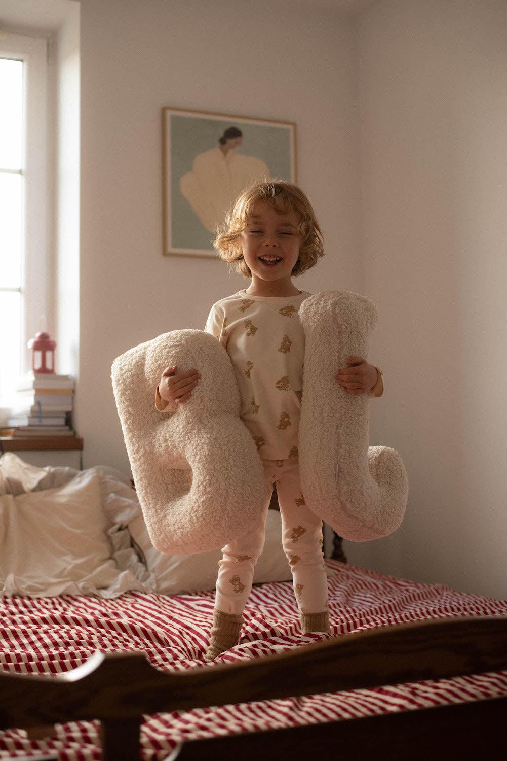 cute little boy with Boucle letter cushion B and J teddy letter pillow by bettys home in his hands standing on bed