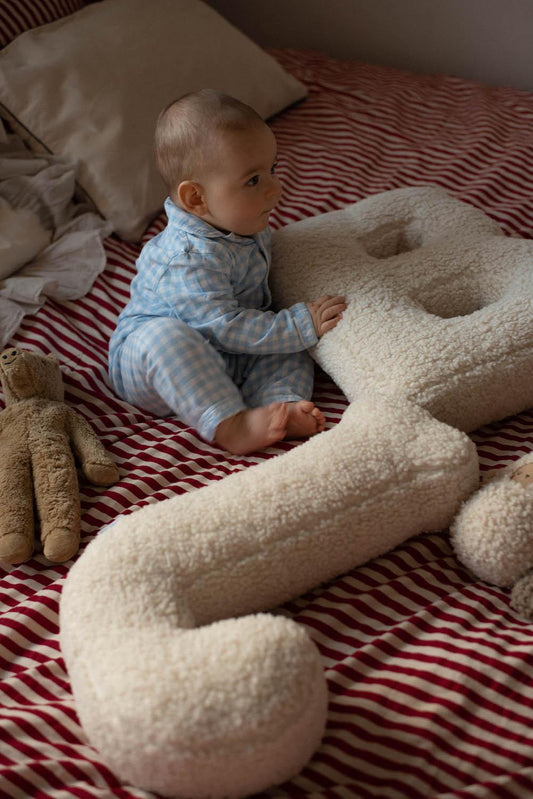 cute baby boy sitting on bed with boucle letter cushion B and J by bettys home as kids bed decoration