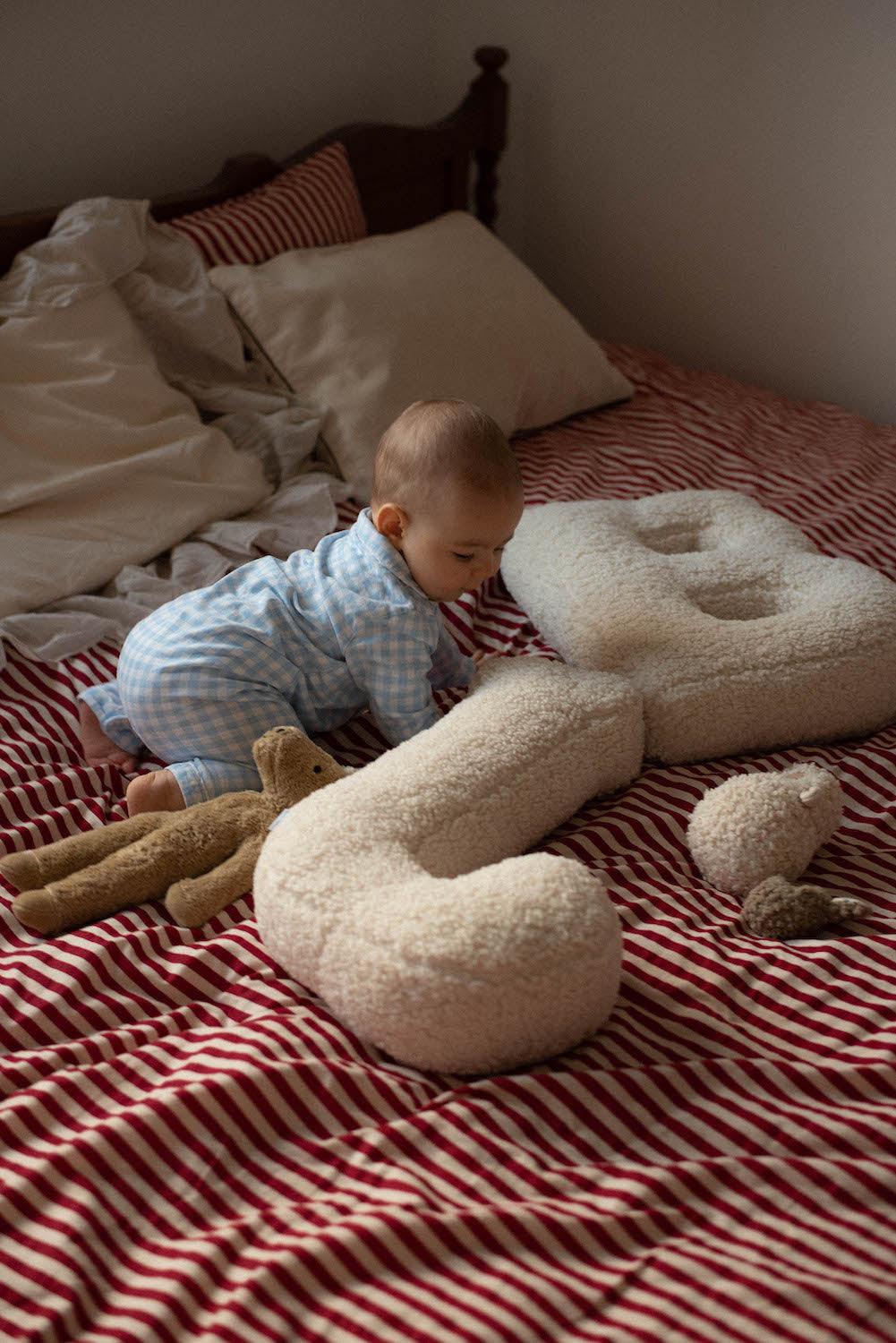 baby boy on bed next to Boucle letter cushion J and B teddy pillow by bettys home kids room decorations 