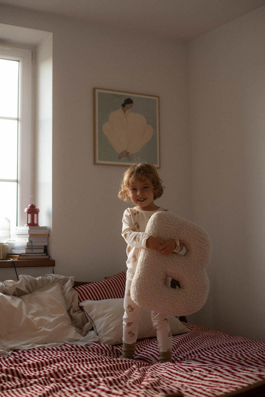 little boy standing on bed with boucle letter pillow B in hands as bedroom decoration idea