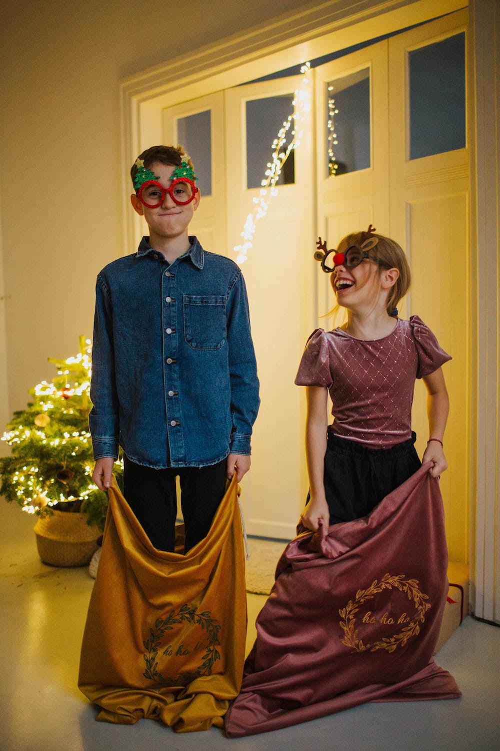 boy and girl standing with velvet christmas sack with embroidered ho ho ho by Bettys Home 