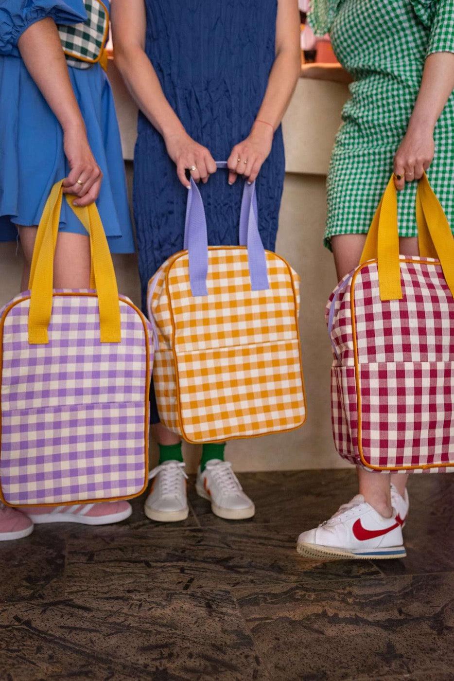 Young women in a restaurant standing with gingham backpacks in their hands. checkered backpacks by bettys home