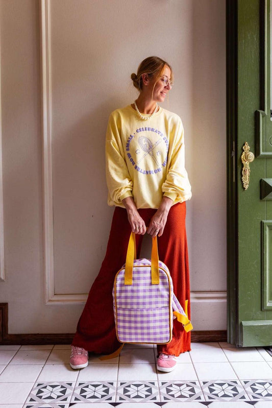 woman standing in hall in yellow blouse with lilac gingham backpack by bettys home in her hands. Beautiful checkered backpack