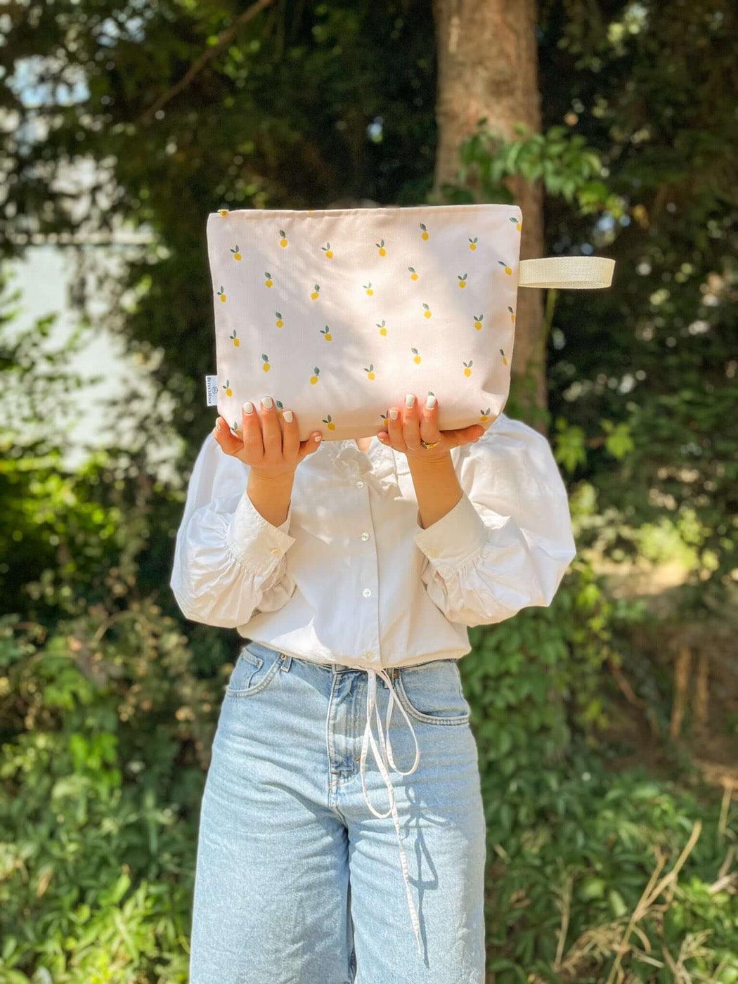 A cosmetic bag for the beach in which to store a wet suit. In the photo it is held by the girl in front of her. The cosmetic bag has lemons printed on it. Cosmetic bags from Bettys Home 