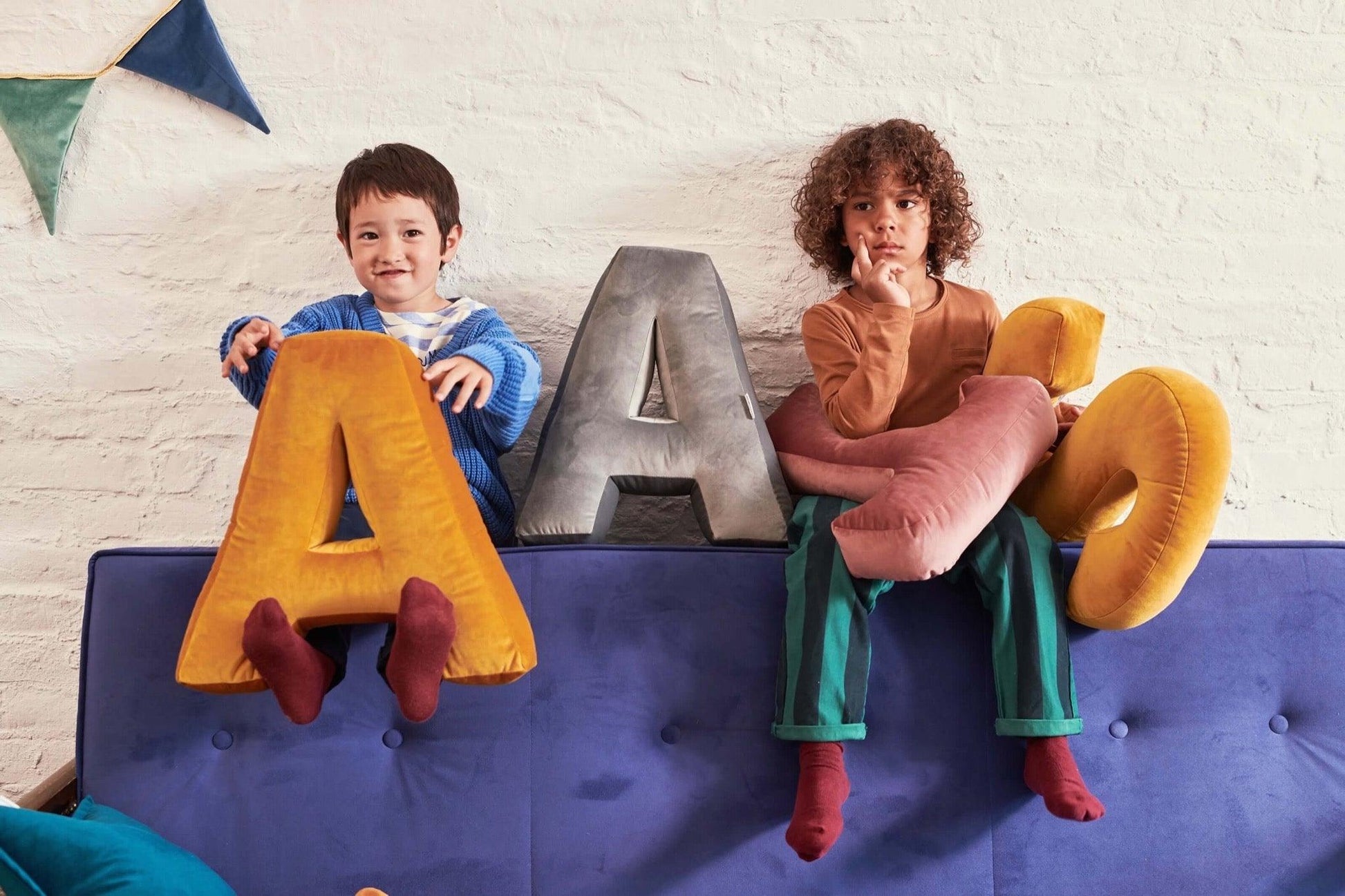 two boys sitting on couch with velvet letter cushions by bettys home