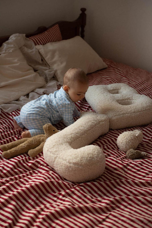 little baby on bed next to Boucle Letter Cushions by Bettys Home