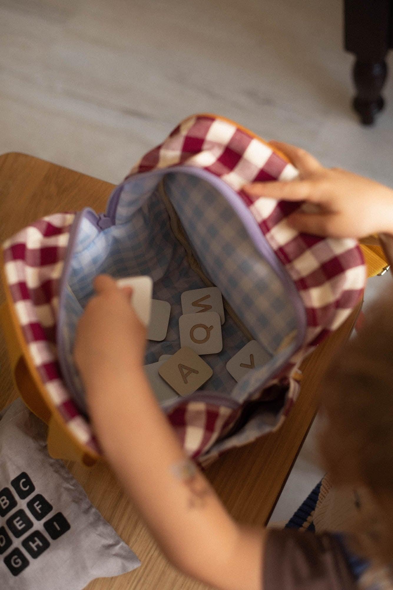 little boy drawing from a small checkered backpack wooden toys. small backpack for kindergarten 