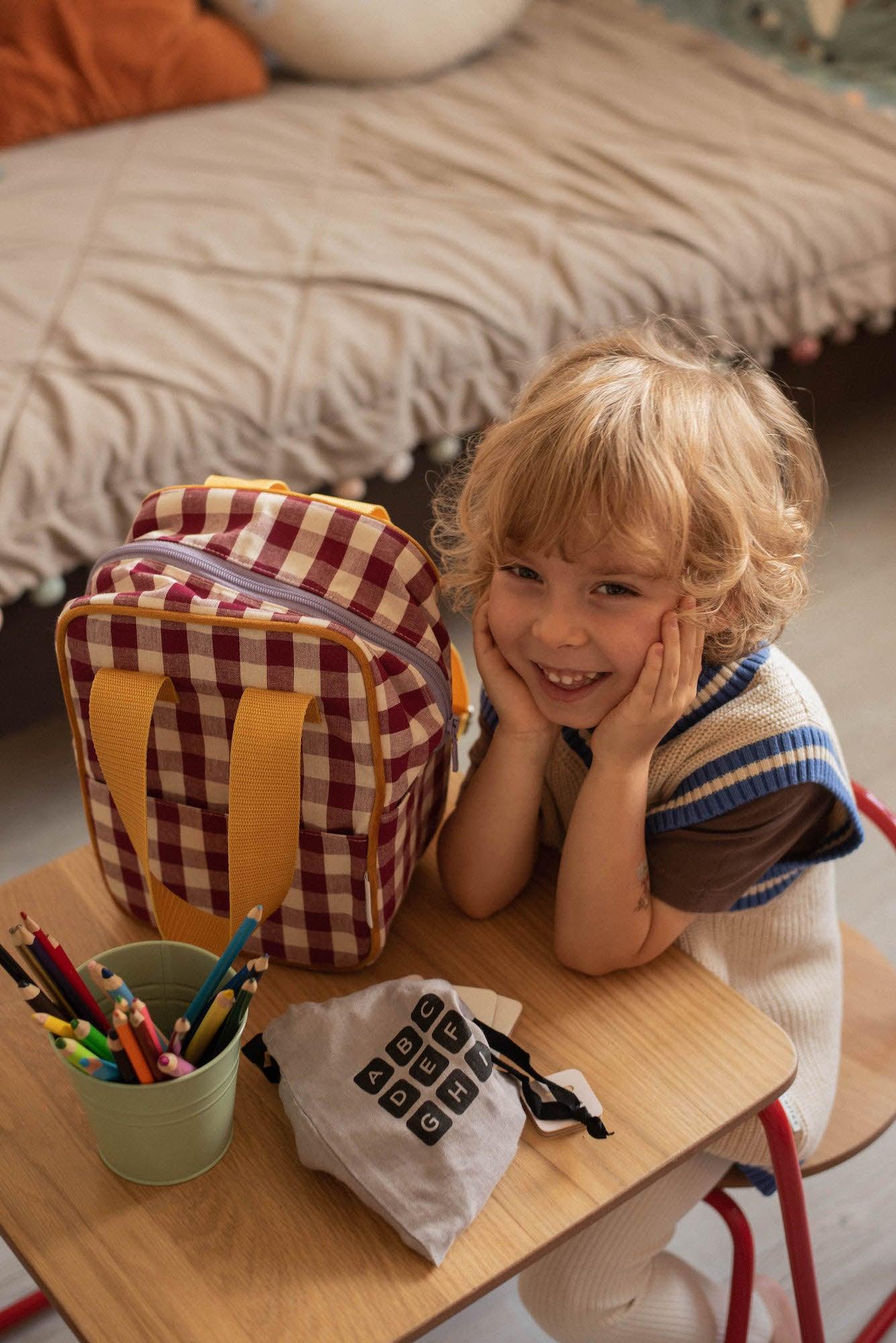 a little boy sitting at a table next to his boys backpack for kindergarten. school backpack for kids