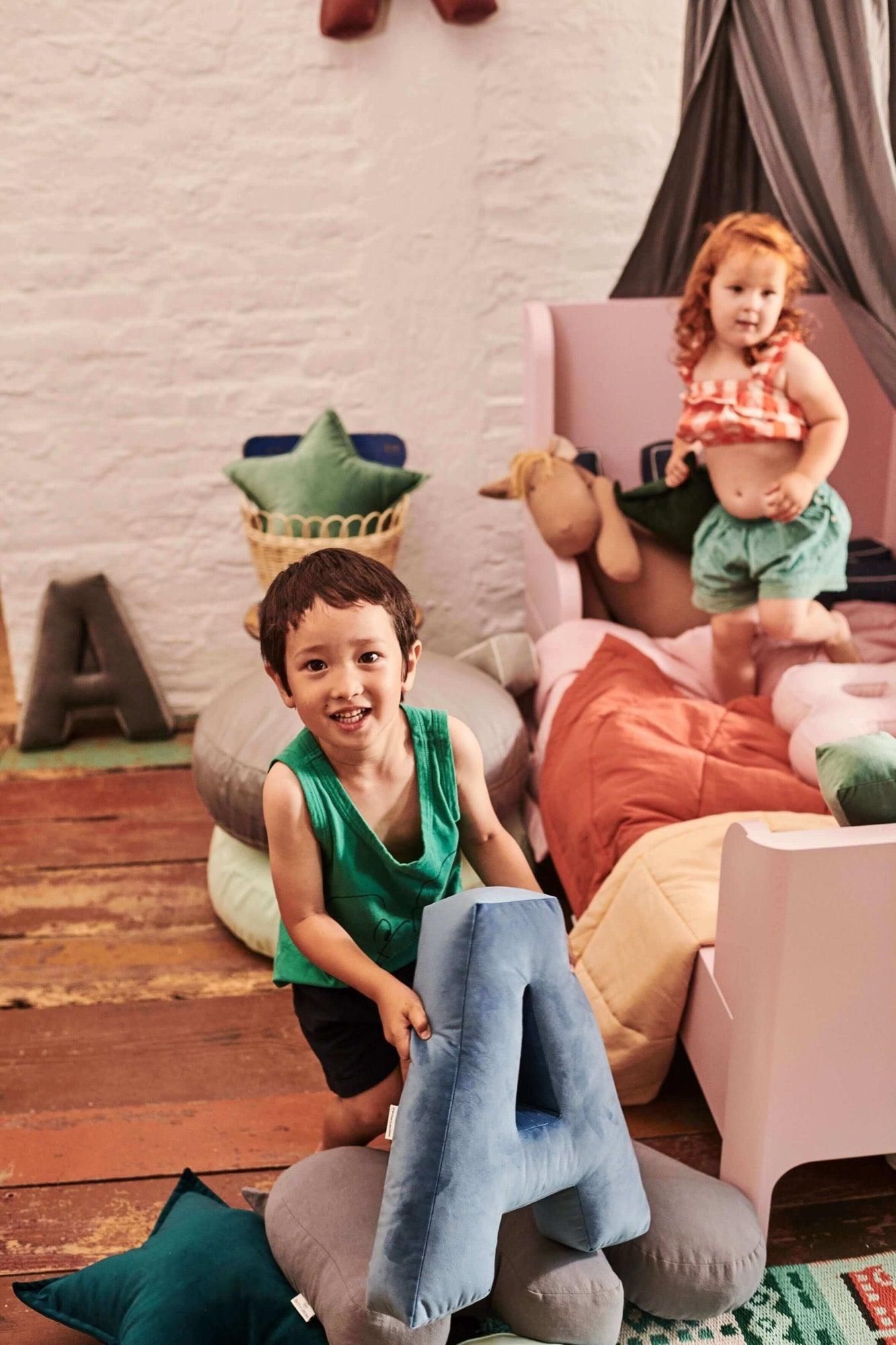 boy holding a velvet letter cushion a in a colorful room against the background of a canopy bed by bettys home