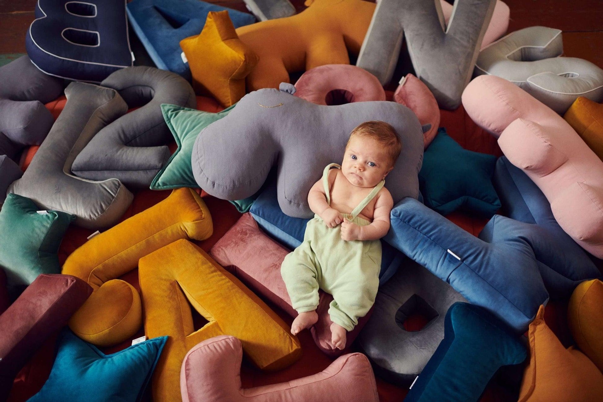 baby boy lies among velvet letter cushions by bettys home and hippo cushion