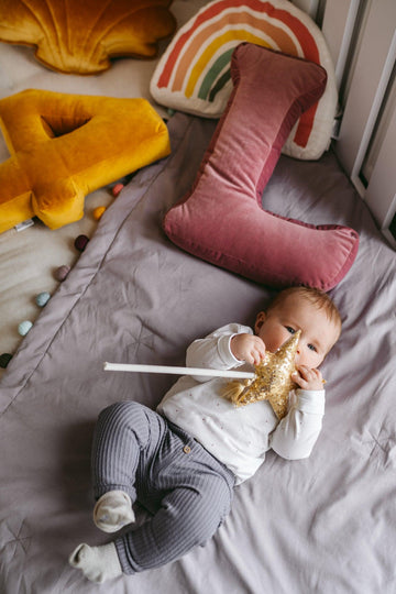 baby girl on bed near to velvet letter cushion L in old rose pink by bettys home