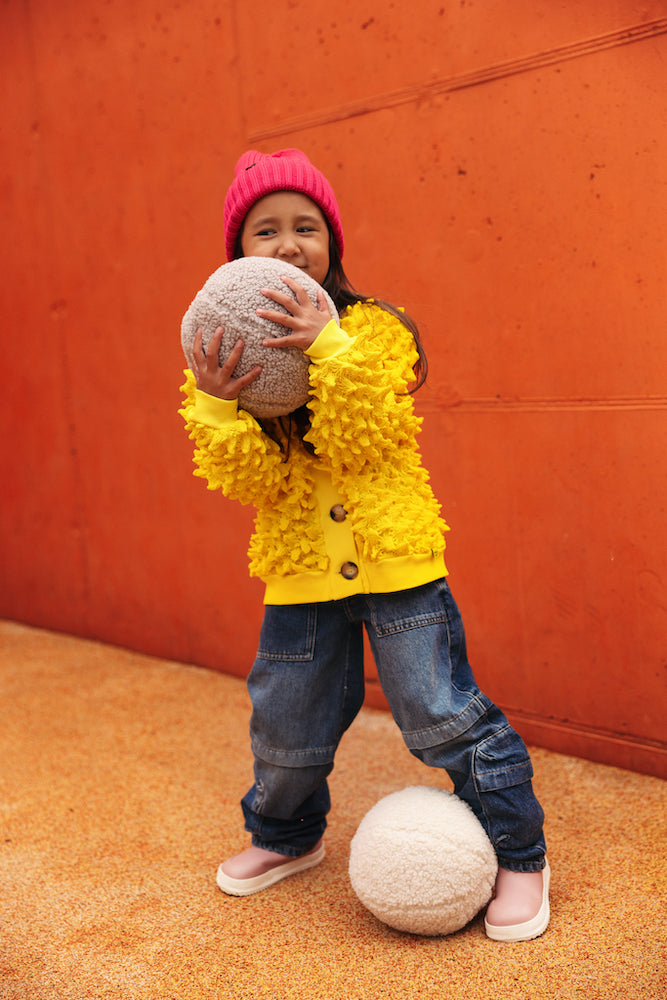 girl in yellow jacket with boucle ball pillow by bettys home. Boucle ball cushion. Ball shaped cushion