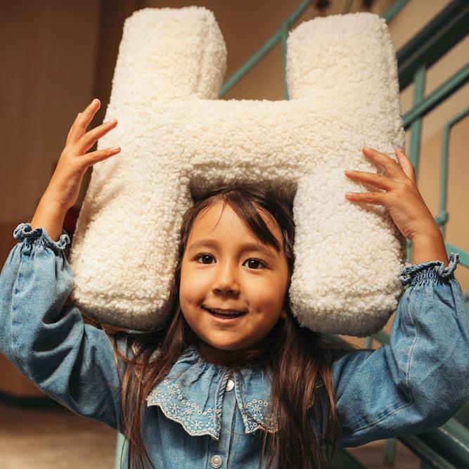 Girl holding boucle letter cushion on head. Boucle letter pillow. teddy pillow