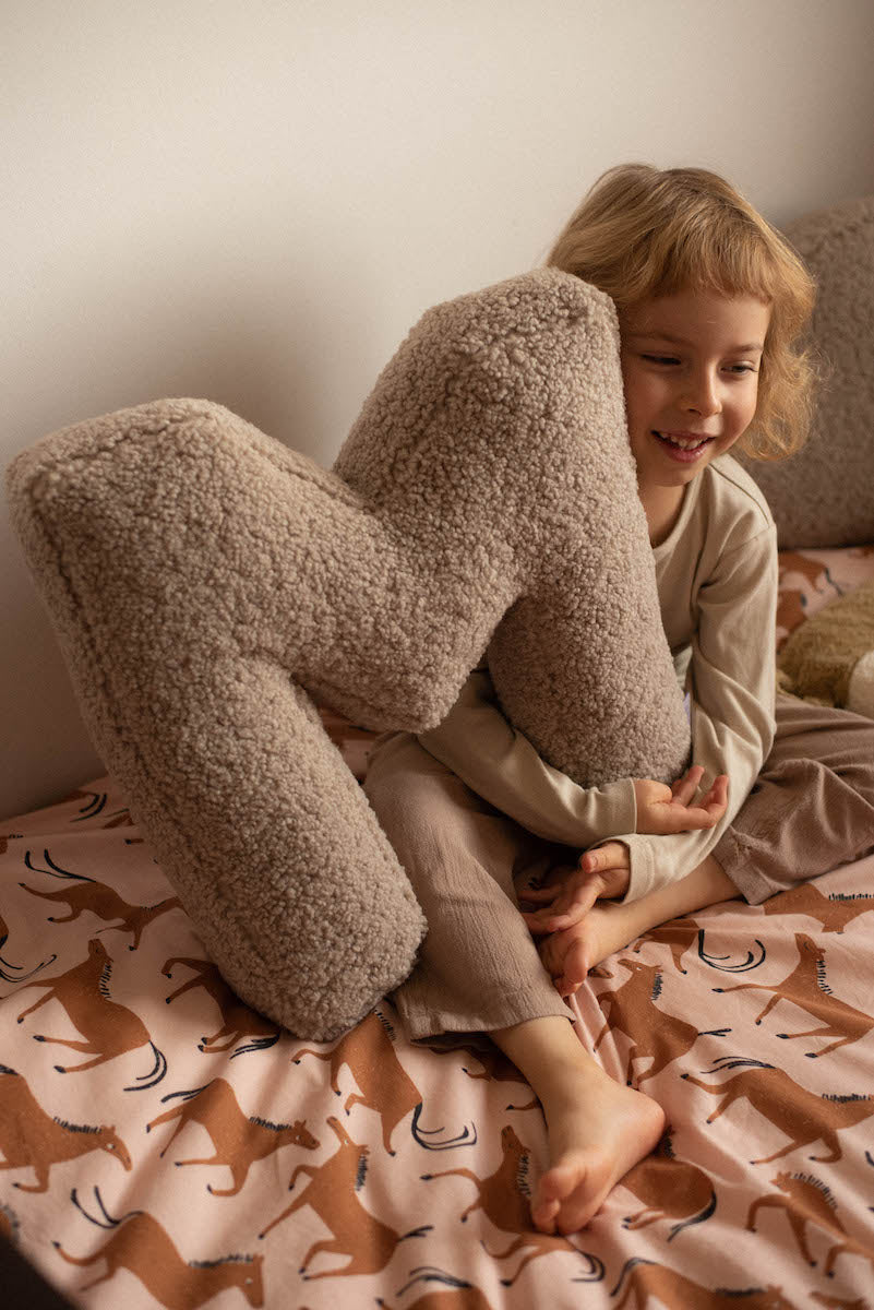 qute boy sitting on kids bed with boucle letter cushion M in hands by bettys home