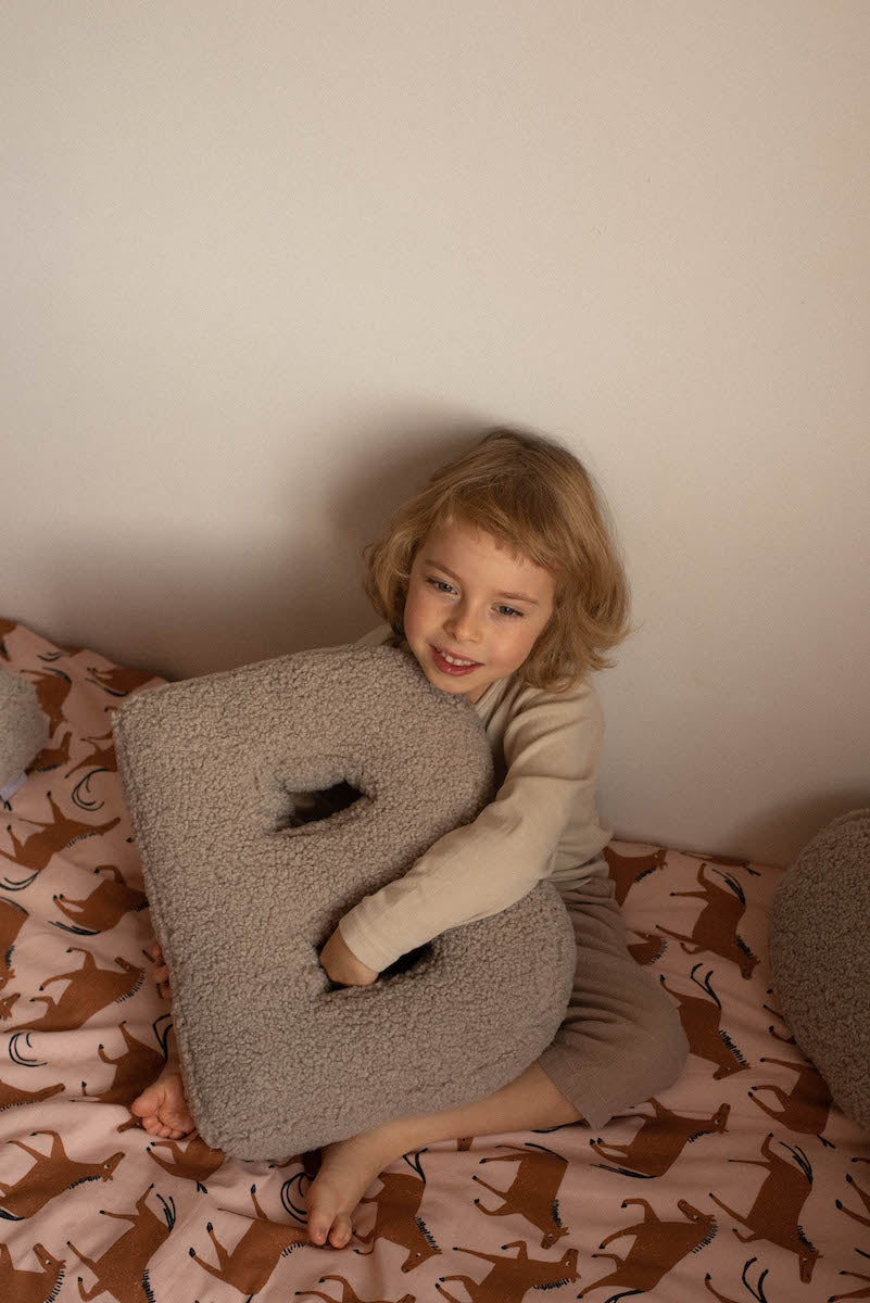 qute boy sitting on bed with boucle letter cushion B by bettys home in hands