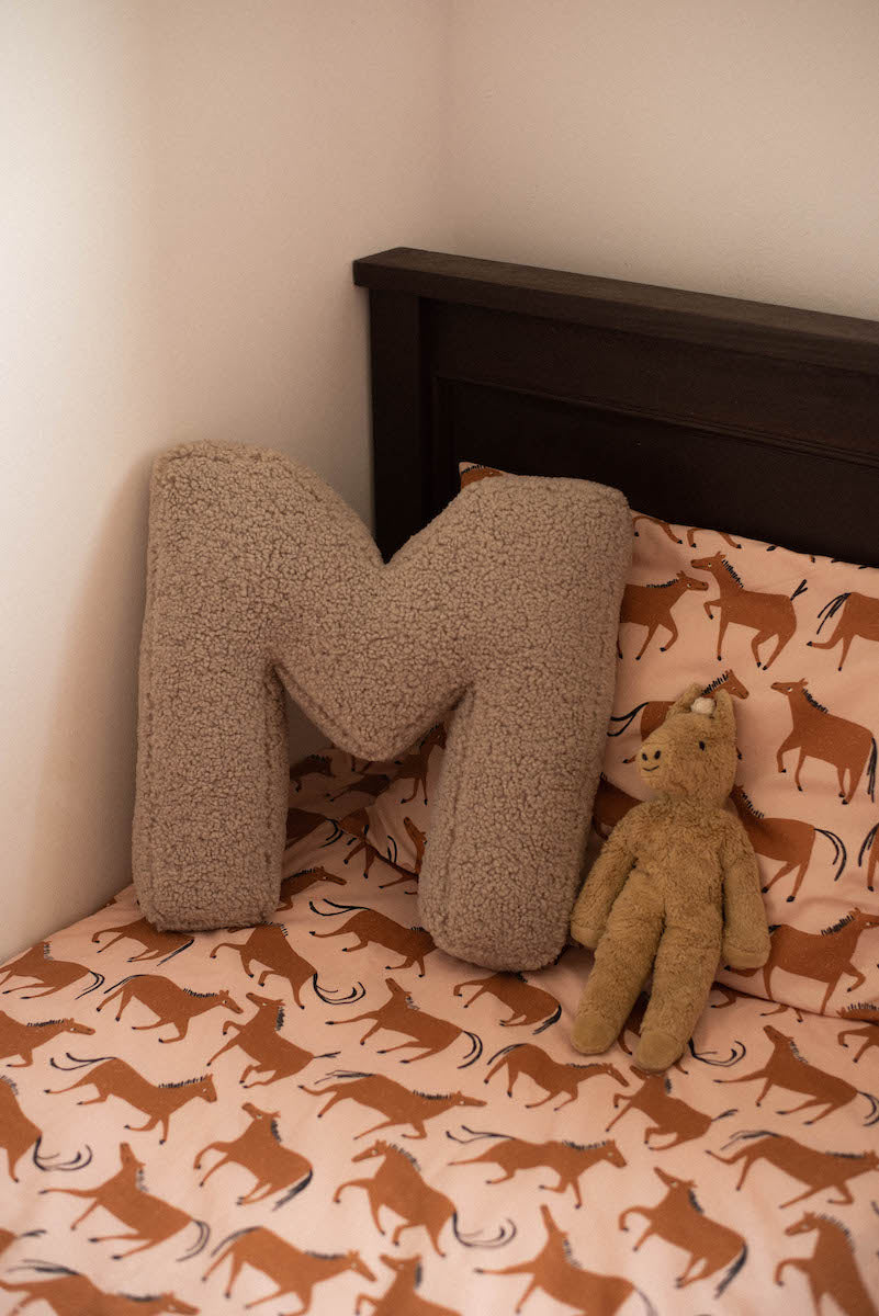 boucle letter cushion M mocha on kids bed. teddy pillow