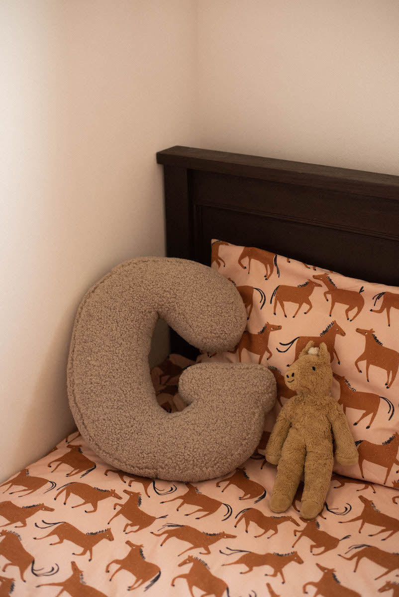 boucle letter cushion g mocha on kids bed. teddy pillow for kids 