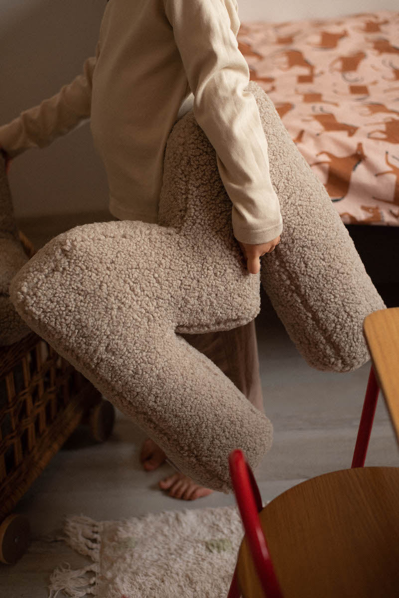 little boy standing with boucle letter cushion M mocha in hands 