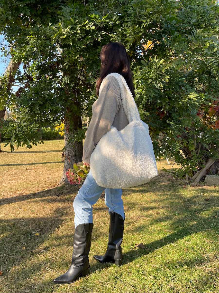 woman in garden next to trees with boucle shopper bag. Fashionable bouclé tote bag for everyday use. boucle tote bag