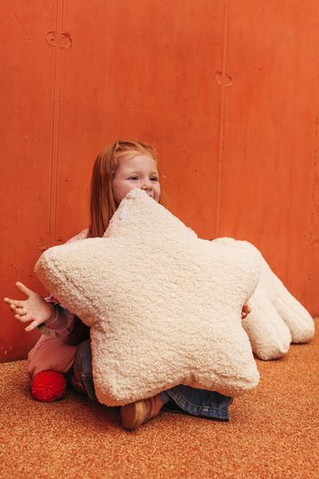 girl on orange background sitting with boucle star cushion by bettys home. Teddy pillow