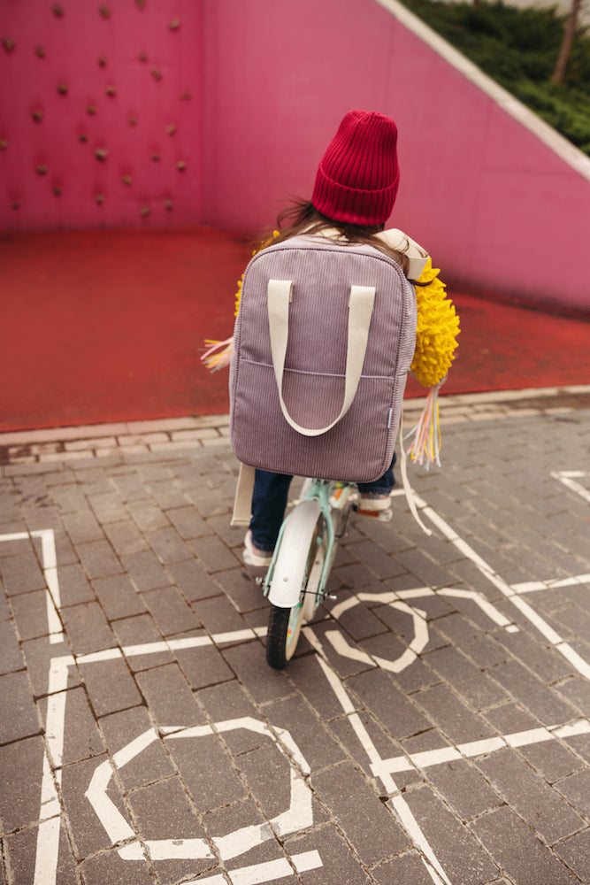 little girl on playground riding bicykle with corduroy backpack in lilac by bettys home