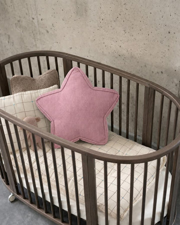 Pink corduroy star cushion styled in oval wooden crib against concrete wall by Bettys Home