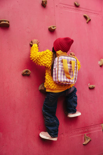 girl climbing a wall in a playground with a gingham backpack by bettys home