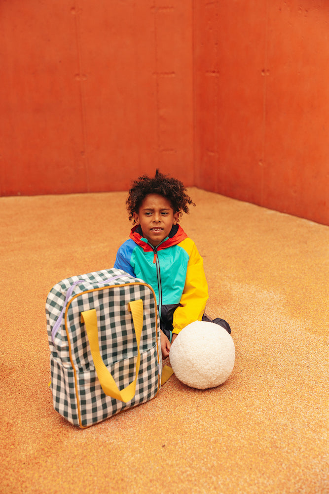 boy sitting on the ground next to a gingham backpack and boucle ball cushion boy bettys home