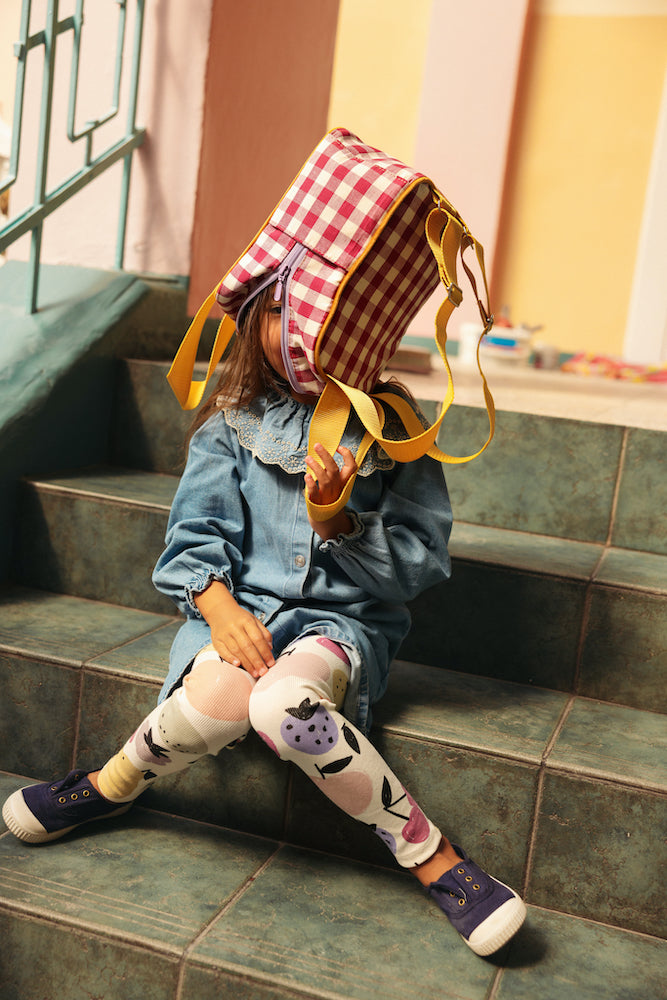 A little girl sitting on the steps at school with gingham backpack by bettys home on her head 