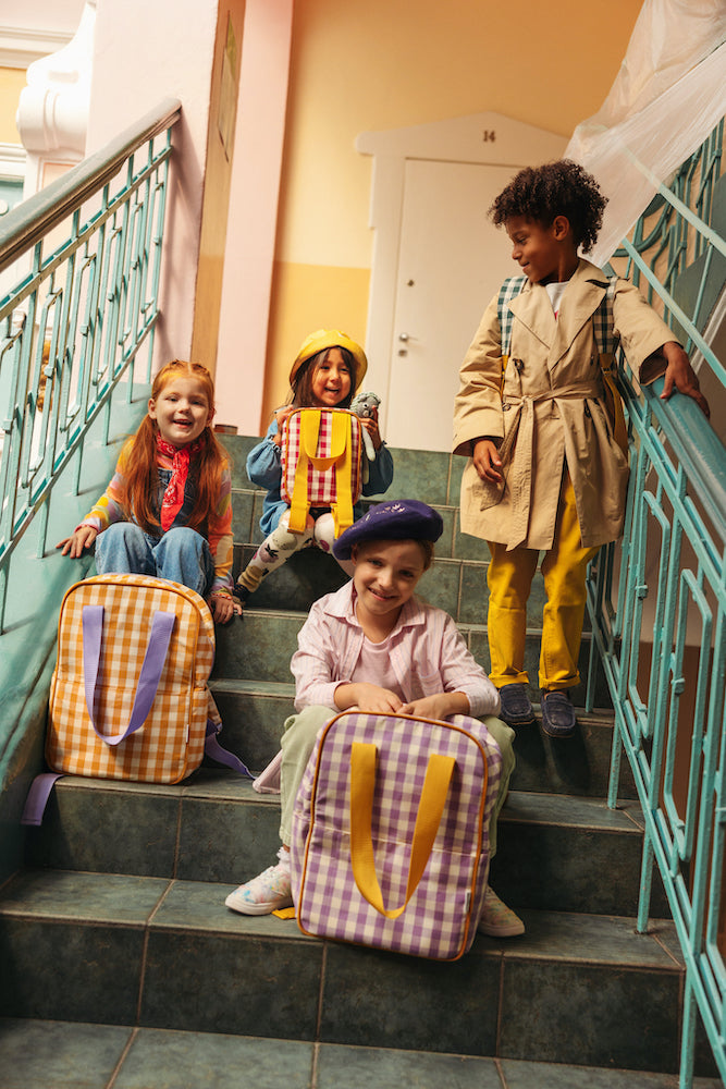 Children sitting on the steps at school with gingham backpacks baby bettys home