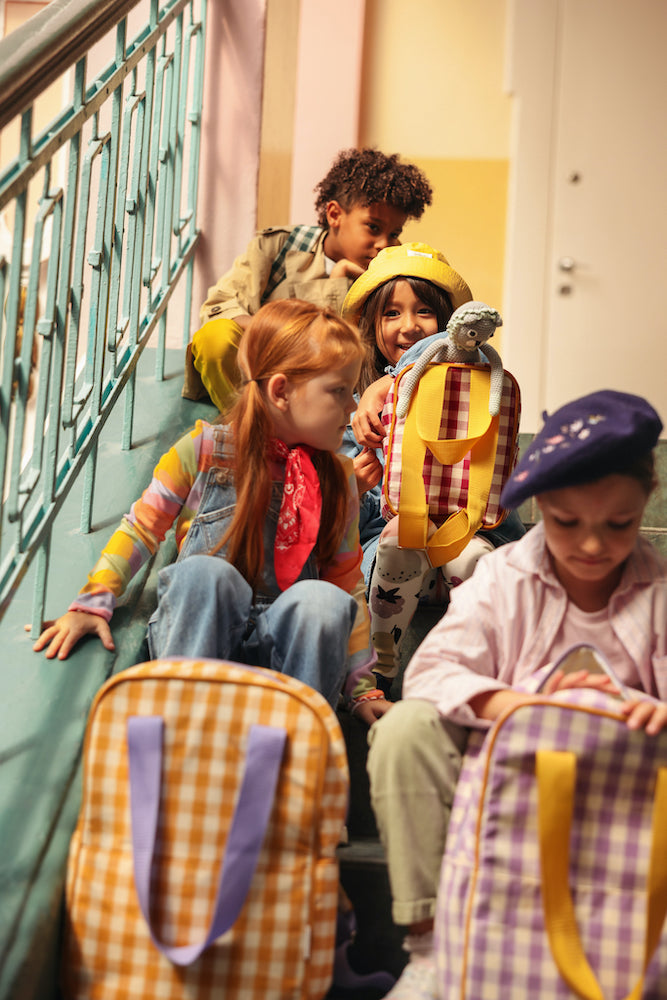 kids sitting at school on stairs with gingham backpack by bettys home at front of them. 