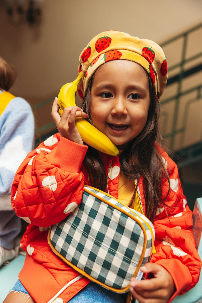 Little pretending to talk through a banana with a green gingham hip pack by bettys home. gingham hip pack