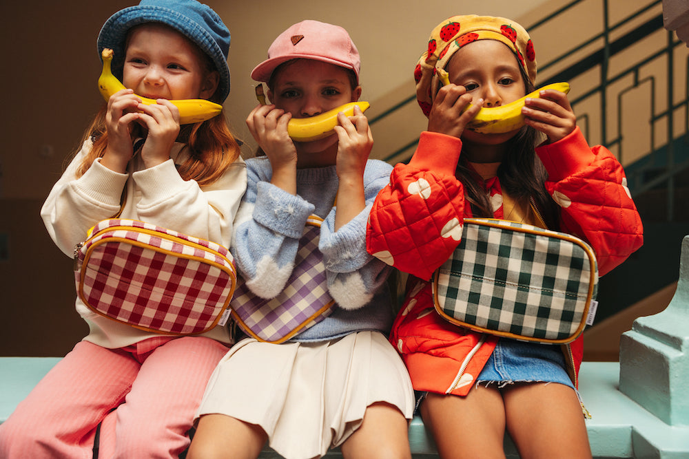 girls sitting on a wall with a banana have gingham hip packs by bettys home. gingham fanny pack. gingham belt bag